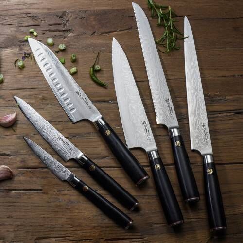 Image of a ProCook Damascus 67 six piece knife set resting flat on wooden surface next to garlic cloves, chopped spring onion and herbs